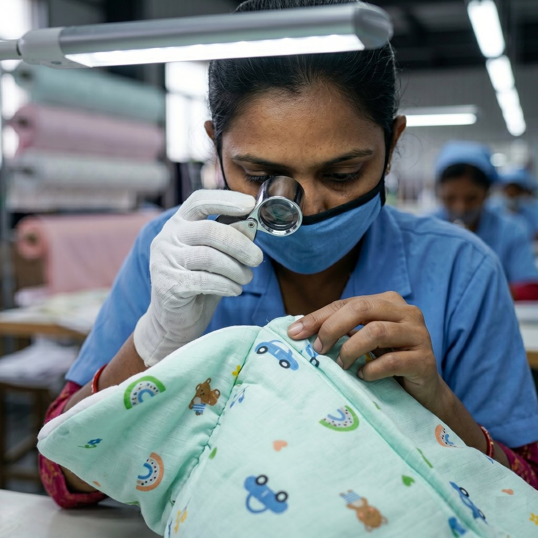 Quality inspector examining a printed muslin baby blanket through a loupe under task lighting